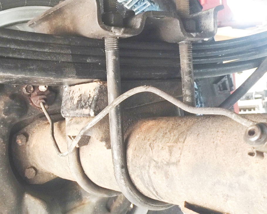 Close-up of vehicle rear axle and leaf spring assembly with brake line.