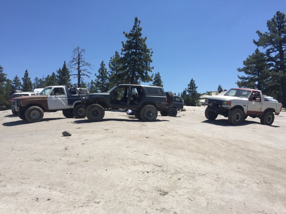 Three modified off-road vehicles parked on a rocky surface.