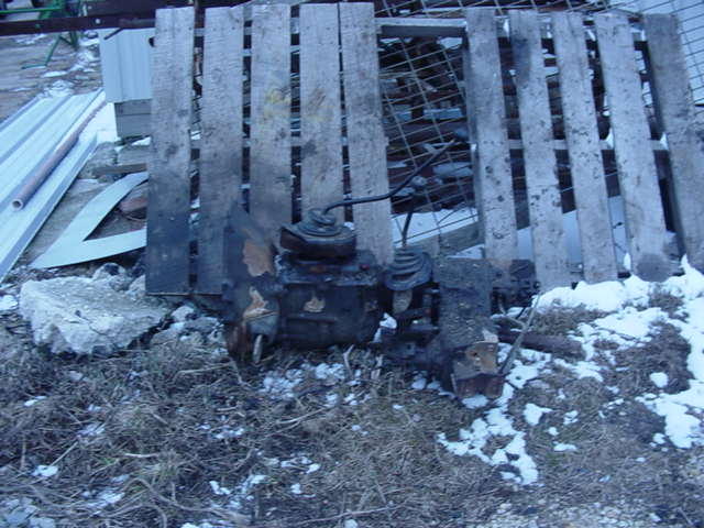 rusted vehicle transmission parts on snowy ground near wooden pallets