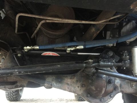 1984 Ford Bronco - Underneath view of a 1984 Ford Bronco showing a hydraulic steering assist cylinder mounted to the front axle and steering linkage. The cyli…