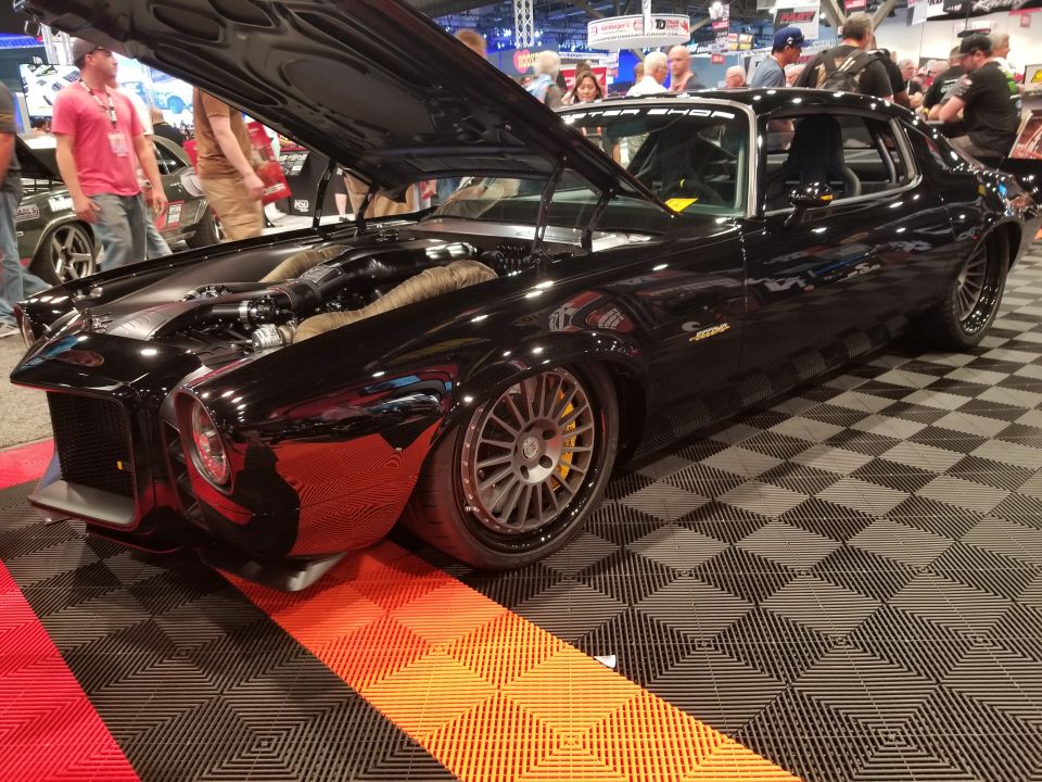 Modified black 1969 Pontiac Firebird with hood open, showing custom engine and wheels.