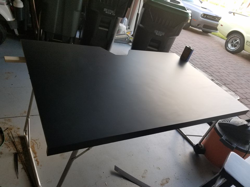 Black dashboard panel on sawhorses in a garage, with trash cans and cars in the background