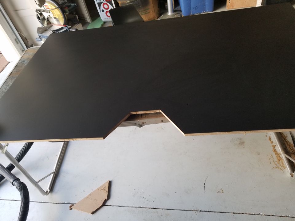 custom cut black wood panel with a notch, resting on sawhorses in a garage
