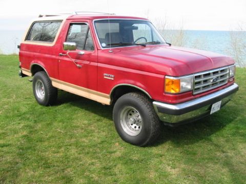 1988 Ford Bronco - This red 1988 Ford Bronco is parked on a grassy area with a body of water in the background.