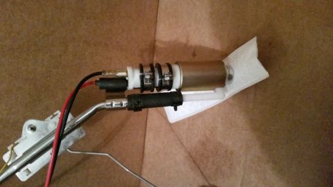 1985 Ford Bronco - A close-up view of a fuel pump assembly with a filter attached. The assembly includes a brass-colored pump, white plastic components, black…