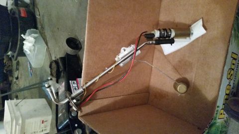 1985 Ford Bronco - A fuel pump and sending unit assembly is shown laid out inside a cardboard box. The assembly includes a metal arm with a float and electric…