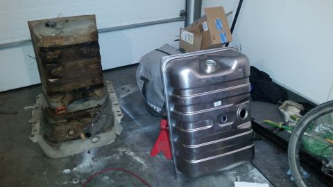 1985 Ford Bronco - A new, shiny metal fuel tank is displayed next to an old, rusty fuel tank in a garage setting. The new tank is supported by a red jack stan…