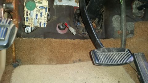 1985 Ford Bronco - The interior driver's side footwell of an older vehicle, showing the fuse box, brake and gas pedals, and wiring.