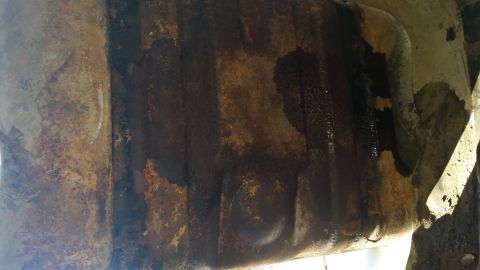 1985 Ford Bronco - Close-up of a badly rusted and stained metal fuel tank or floor pan on the underside of a vehicle.