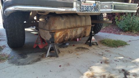 1985 Ford Bronco - The underside of a vehicle shows a large, rusty fuel tank supported by jack stands. A license plate reading "WASHINGTON 6 B38765" is visibl…