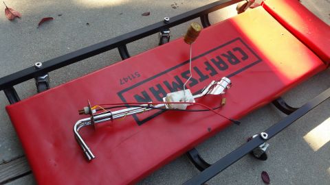 1985 Ford Bronco - A fuel sending unit with a float is resting on a red Craftsman creeper, which is on a concrete surface.