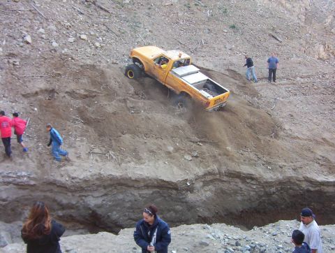 2000 Ford F-450 - A yellow lifted regular-cab pickup climbing a steep dirt embankment at an off-road park, front wheels crested and a rear tire throwing dust…