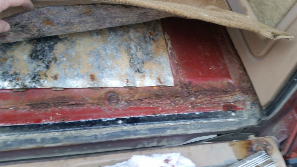 Close-up of severe rust on a vehicle floor pan under pulled-back carpet.