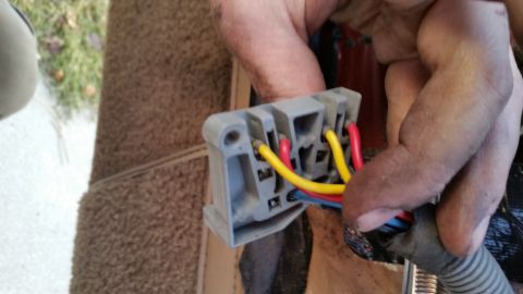 1985 Ford Bronco - A close-up shot shows a person's hands holding a gray electrical connector with red, yellow, and blue wires connected to it. The connector…