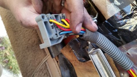 1985 Ford Bronco - A person's hands are holding a gray electrical connector with red, yellow, and blue wires connected to it. The connector is part of a large…