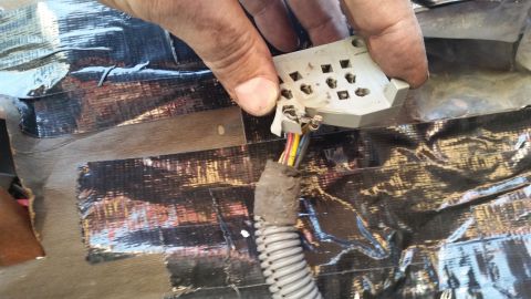 1985 Ford Bronco - A hand holds a white plastic electrical connector with multiple pins and wires attached. The connector is positioned over a surface covered…