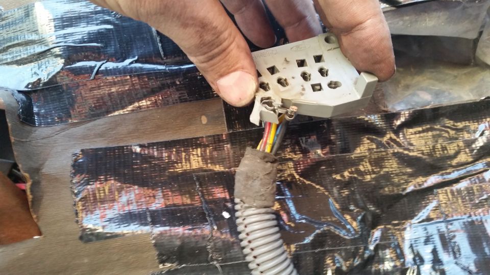 Hand holding a car electrical connector with wires over a taped surface
