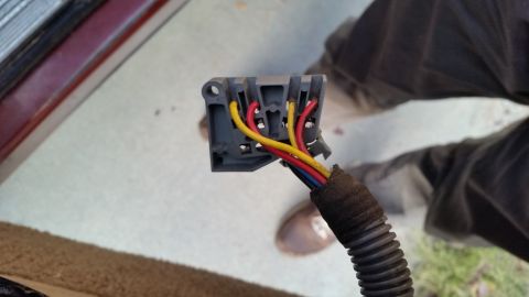 1985 Ford Bronco - A close-up view shows a gray electrical connector with red, yellow, and blue wires. The connector is attached to a black corrugated wire lo…