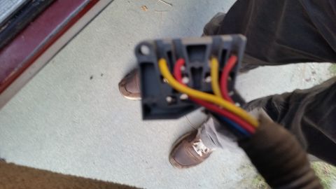 1985 Ford Bronco - A close-up view of a gray electrical connector with red, yellow, and blue wires attached. The connector is held in front of a person's legs…