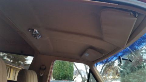 1985 Ford Bronco - The interior of a vehicle's headliner shows a dome light fixture and a sun visor. The view looks towards the front windshield and the exter…