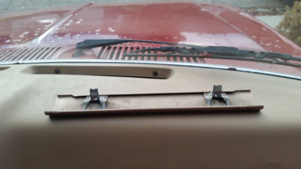 Tan dashboard with a metallic bracket on a recessed panel, hood and windshield wipers in background.