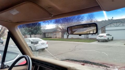 1985 Ford Bronco - Interior view from the driver's seat of a red vehicle looking out the windshield at a suburban street. A cracked windshield is visible, alo…