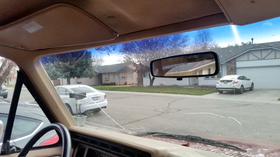 Interior view of a red vehicle with a cracked windshield, looking out at a suburban street with houses and cars.