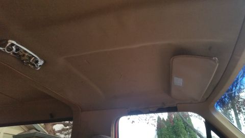 1985 Ford Bronco - The interior of a vehicle's headliner shows a tan sun visor and a chrome dome light fixture. The headliner appears to be sagging in some ar…