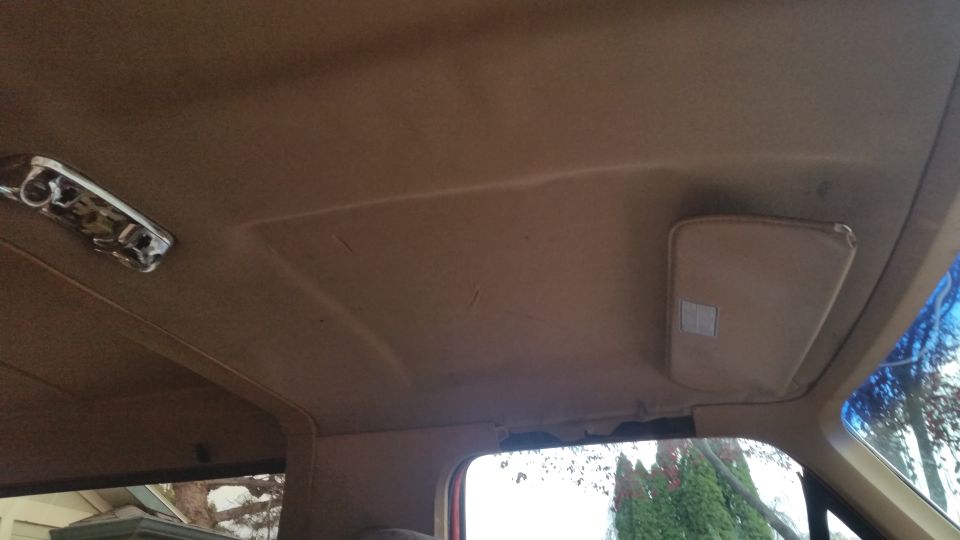 Interior vehicle headliner with tan sun visor and chrome dome light.
