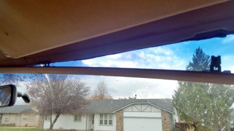 1985 Ford Bronco - View from inside a vehicle looking out through the windshield at a suburban neighborhood with houses and trees. The sun visor is partially…
