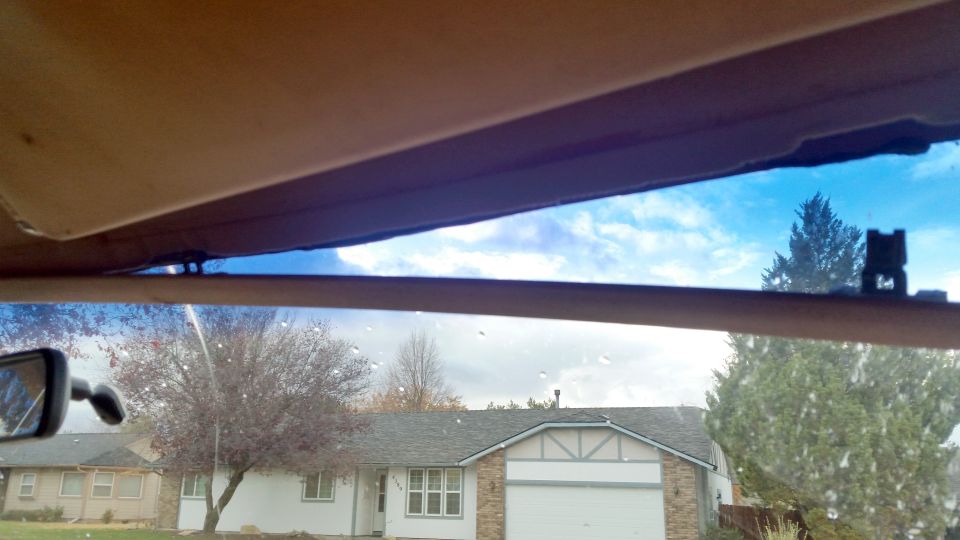 View through a car windshield at houses and trees, with the sun visor visible.