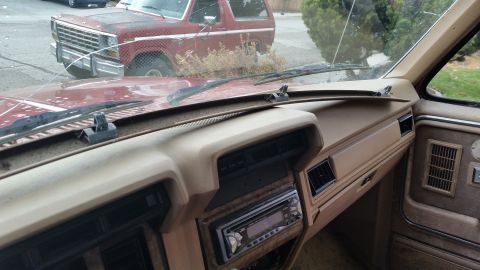 1985 Ford Bronco - The interior of a vintage Ford Bronco shows a tan dashboard with a JVC stereo and air vents. Outside the windshield, the front of another r…