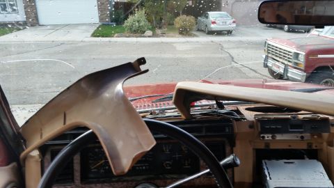 1985 Ford Bronco - Interior view of a tan and red dashboard with a cracked windshield. A red Ford truck is visible through the windshield.