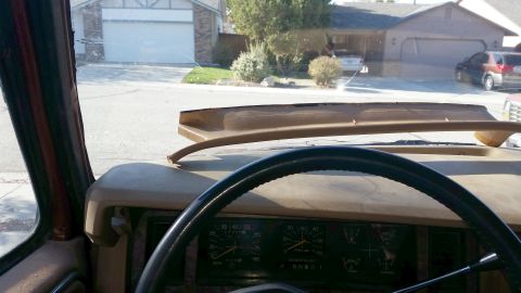 1985 Ford Bronco - Interior view of a vehicle's dashboard and steering wheel, with a cracked windshield showing a residential street and houses outside. A bro…