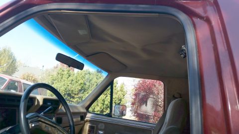 1985 Ford Bronco - Interior view of a vintage Ford Bronco, looking through the driver's side door and windshield. The image shows the steering wheel, dashboar…