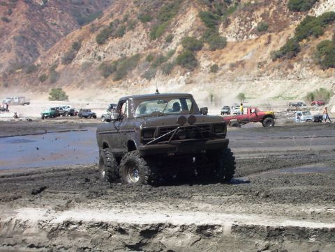 2000 Ford F-450 - A lifted late-1970s Ford Bronco caked in gray mud crawls through a mud pit at an off-road park, running a front brush guard with round auxi…