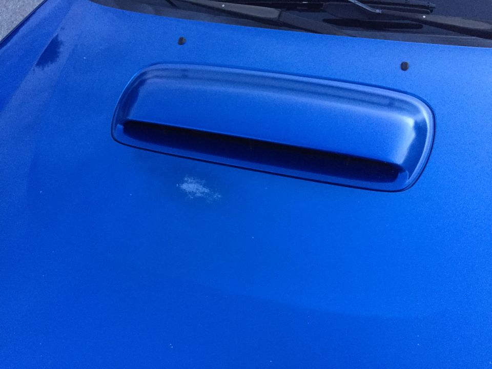 Close-up of blue Subaru Impreza hood with scoop and paint damage.