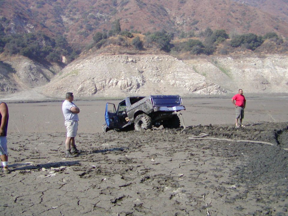 Blue doorless lifted pickup stuck in a mud hole on a dry lakebed with onlookers