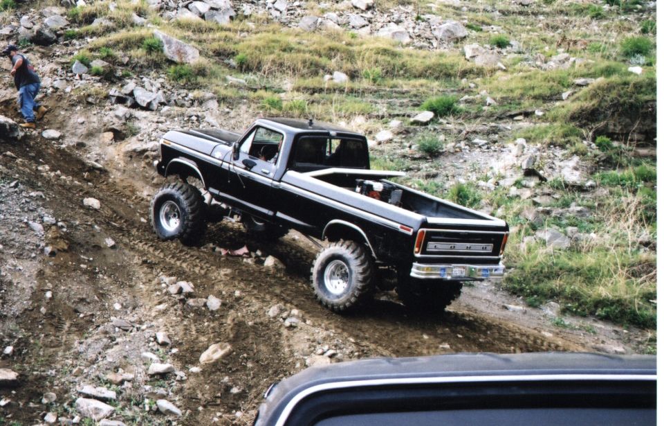 Black lifted Ford pickup on mud tires crawling down a rocky off-road trail
