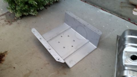 1985 Ford Bronco - A metal fuel tank and its mounting bracket are shown on a concrete surface.