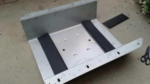 1985 Ford Bronco - A metal skid plate, likely for a gas tank, sits on a concrete surface with rubber isolators and mounting hardware visible.
