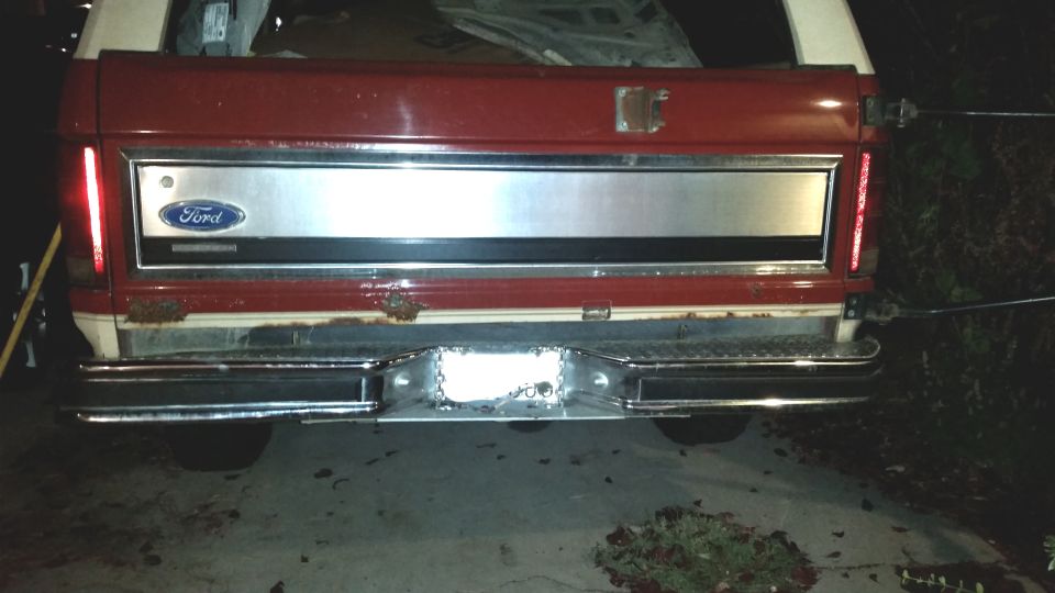 Rear view of a red and white Ford Bronco with a chrome bumper and Ford logo on the tailgate.