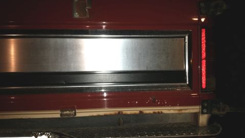 1985 Ford Bronco - The rear passenger side of a red 1980s Ford Bronco is shown, featuring a brushed metal accent panel and a vertical red reflector. The lower…