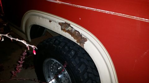 1985 Ford Bronco - The fender of a red SUV shows extensive rust damage around the wheel well, indicating a need for repair.