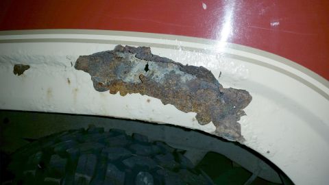 1985 Ford Bronco - Significant rust damage is visible in the wheel well of this vehicle, which is painted red and white.
