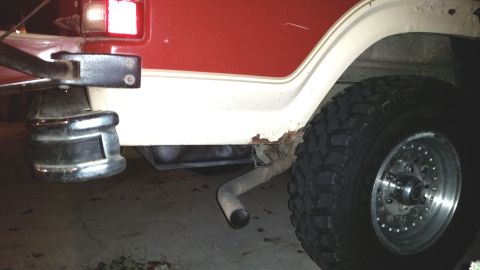 1985 Ford Bronco - Vehicle's rear quarter panel shows rust damage and a visible exhaust pipe and tire.