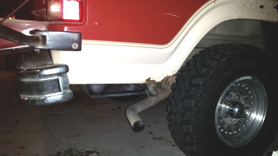 Rear quarter panel of a vehicle with rust near the wheel well, showing a tire and exhaust pipe