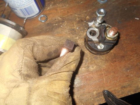 1992 Ford Bronco - A gloved hand holds a copper starter solenoid terminal. Another part of the solenoid is visible on the workbench.