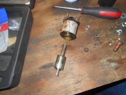 1992 Ford Bronco - Disassembled starter solenoid and plunger components are laid out on a wooden surface alongside a screwdriver and various nuts and washers.