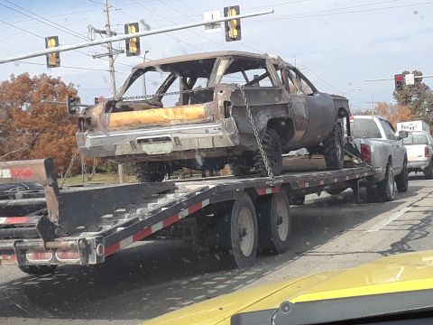 1994 Ford Bronco - A heavily damaged car body is transported on a trailer, showing significant destruction.